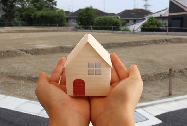 家の模型を持つ手元と空き地の背景